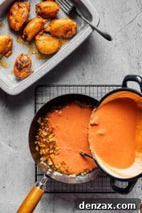 Chopped onions in a skillet. Peanut sauce is being poured over the onions, and a platter of cooked chicken sits nearby.