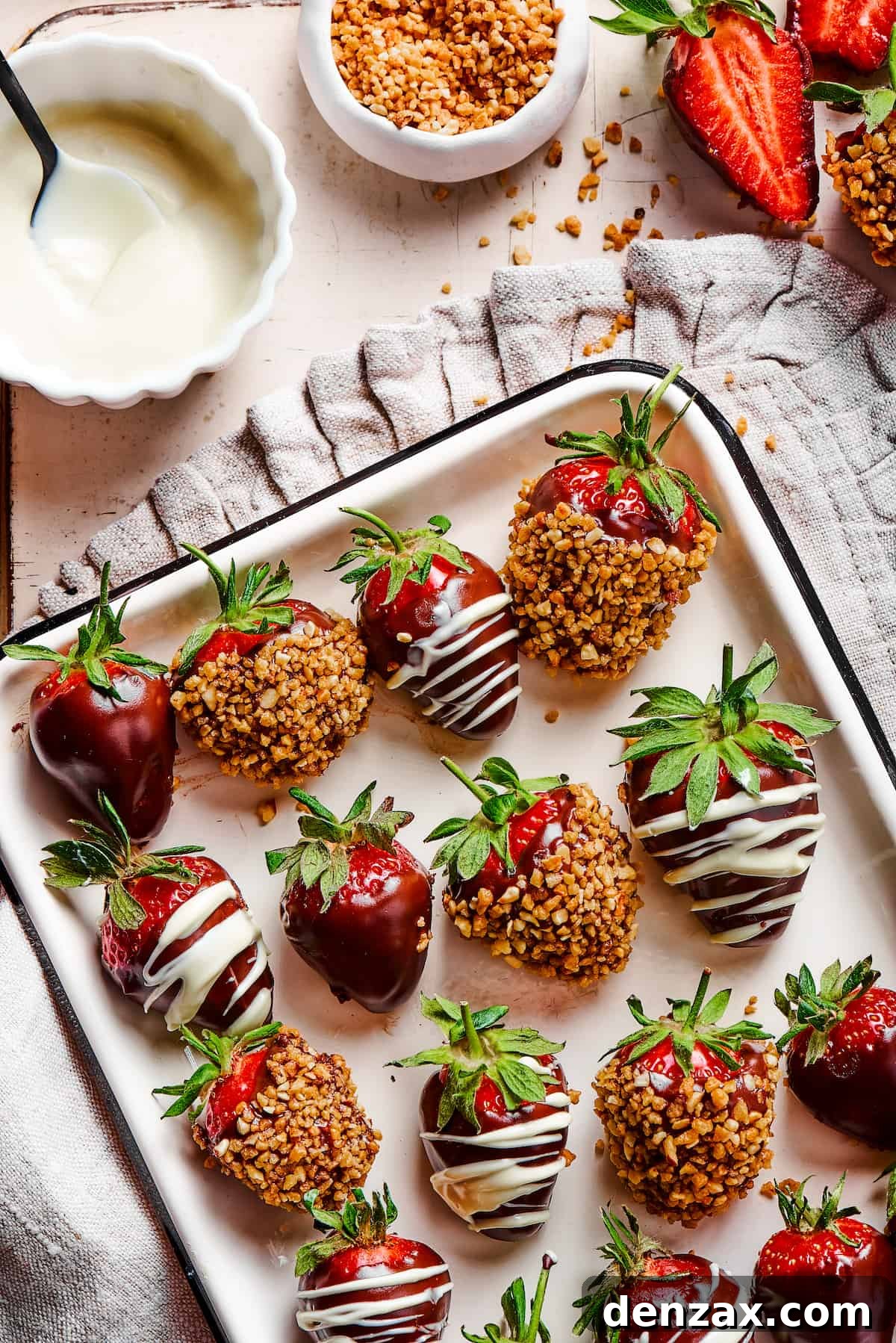 A white tray with a black border, displaying three kinds of chocolate dipped strawberries: plain, white chocolate drizzle, and toasted hazelnuts.