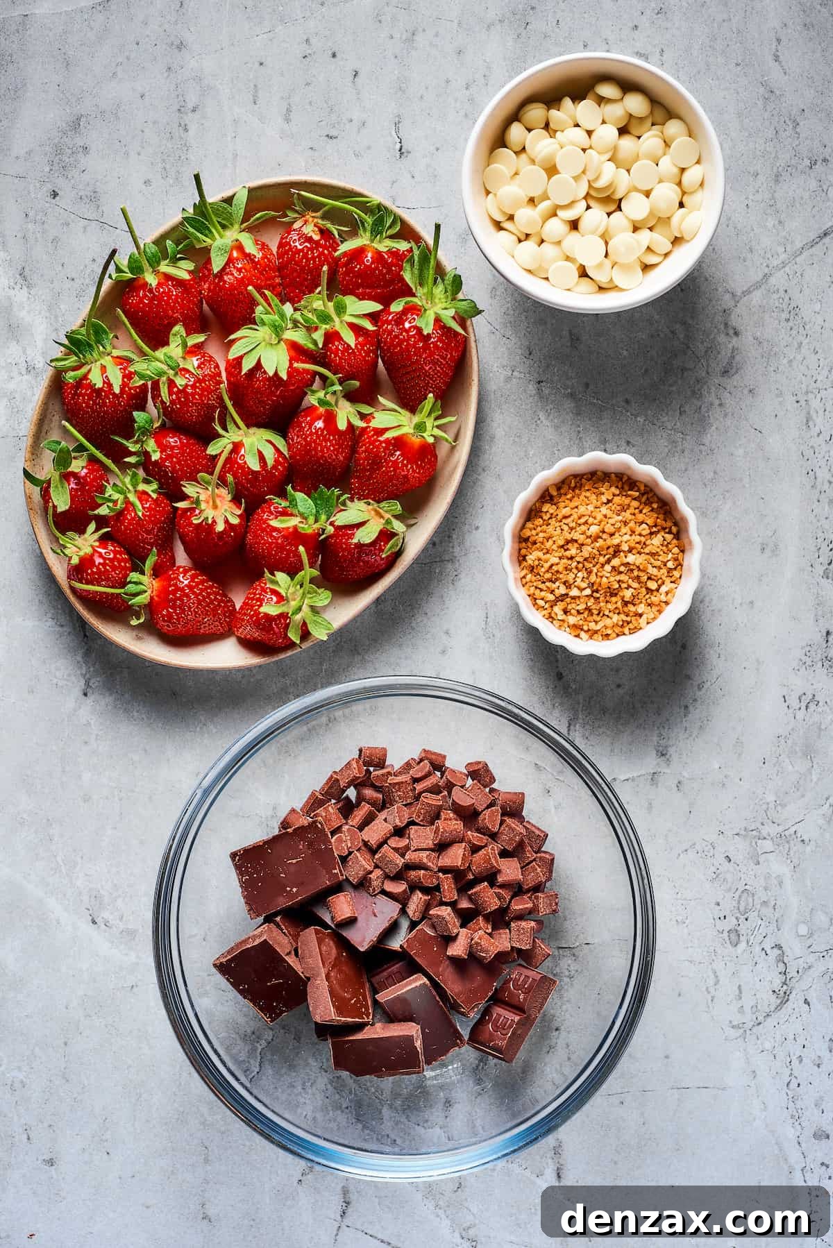 From top left: Fresh strawberries with stems, white chocolate chips, toasted chopped hazelnuts, and bowl with chopped semisweet chocolate and milk chocolate chips, ready for making chocolate covered strawberries.