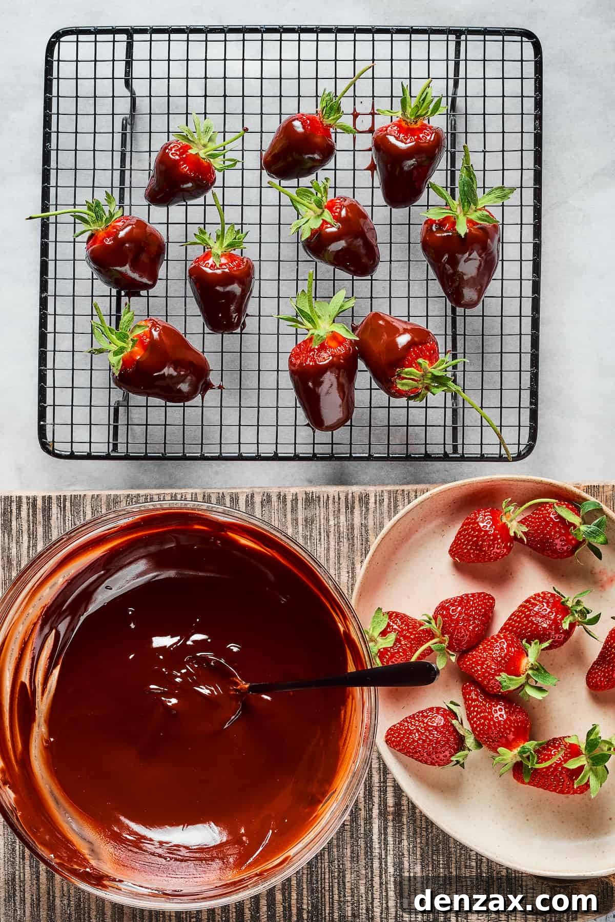 An arrangement of fresh strawberries, a bowl of melted chocolate, and a wire rack with freshly dipped chocolate covered strawberries resting on it to set.