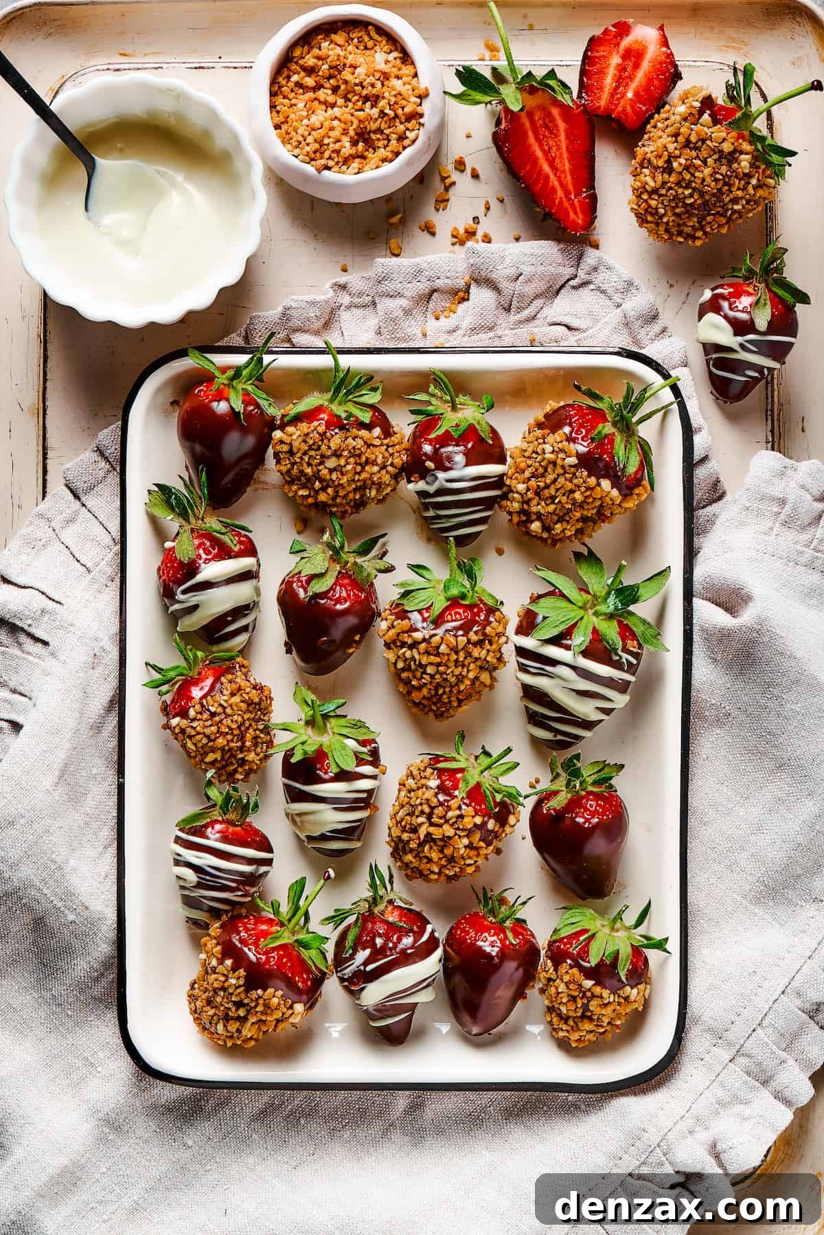 Chocolate covered strawberries on a tray, set on a decorative cloth dishtowel next to a bowl of white chocolate.