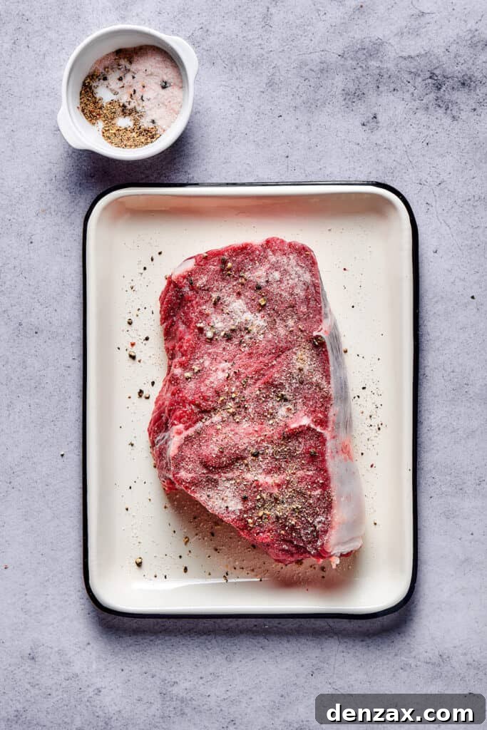 A thick sirloin steak generously seasoned with salt and pepper, ready for searing in an enamel pan.