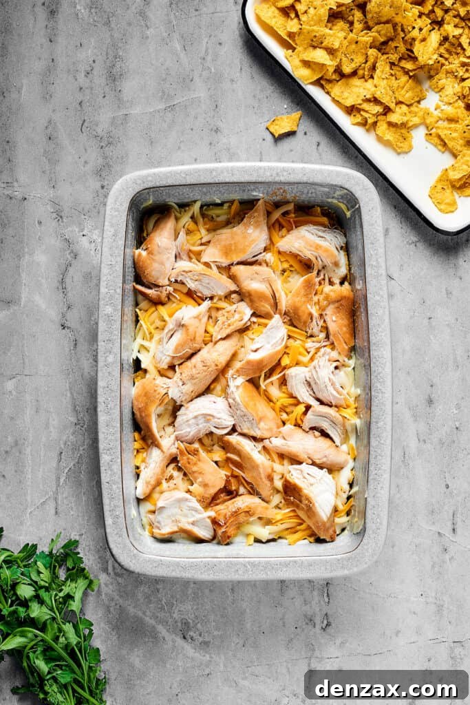 Cheese and chicken layered over other ingredients in a baking dish.
