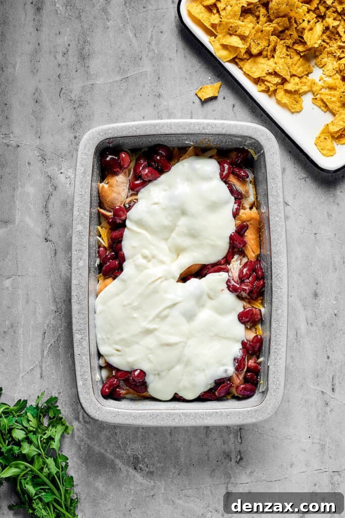 Beans, white sauce, chicken, and other ingredients layered in a rectangular pan.