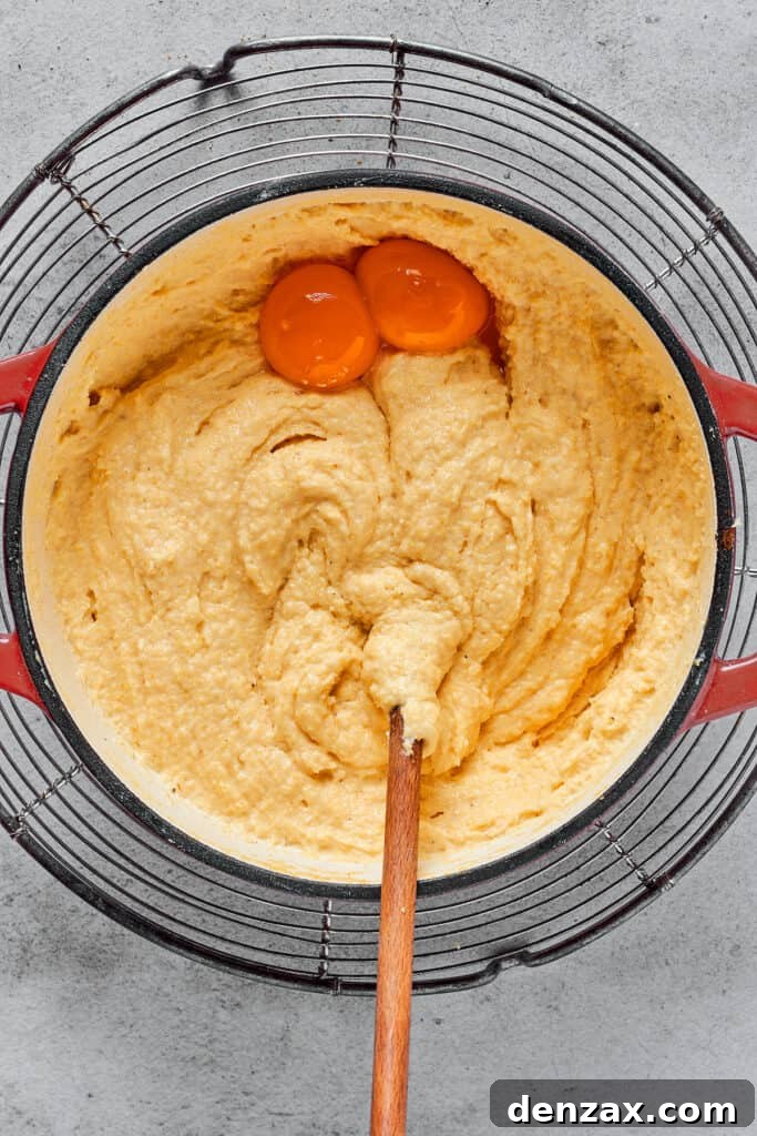 Creamy semolina batter with two egg yolks being stirred in.