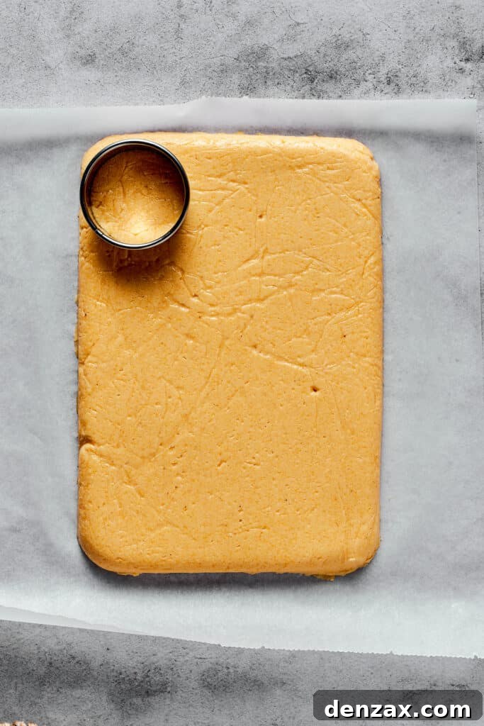 A flat, rectangular sheet of semolina dough on a cutting board, with a circular cookie cutter resting on the dough.