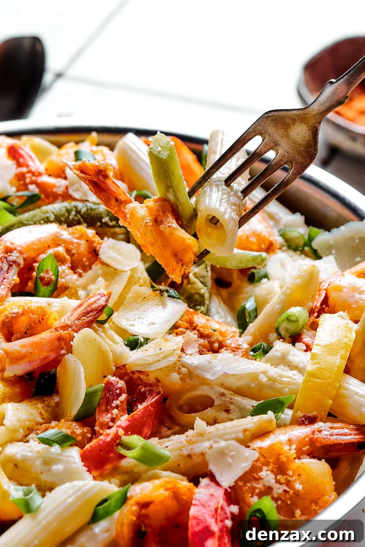 A fork lifting a mouthful of Rasta Pasta with shrimp and bell peppers from a creamy dish.