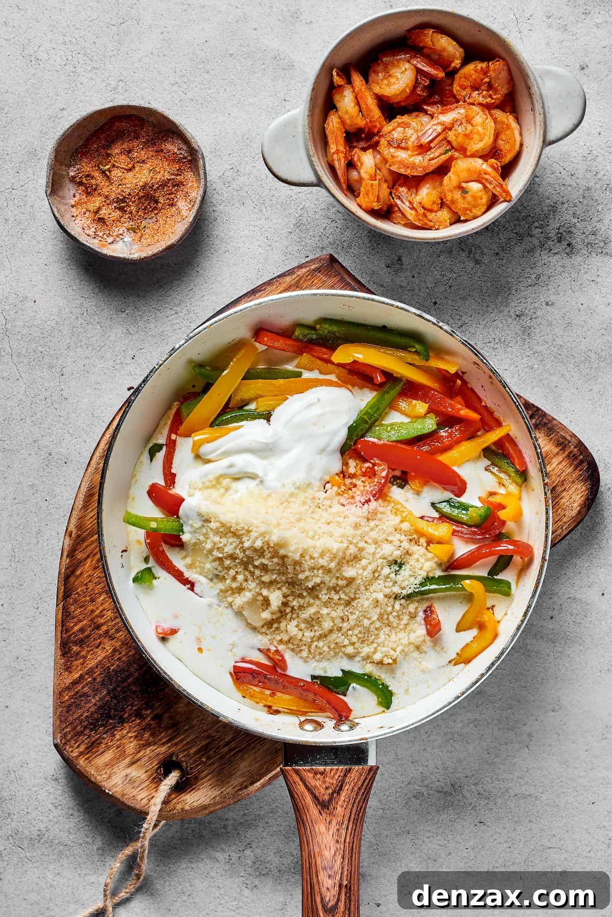 Bell peppers, parmesan, heavy cream, and cream cheese being stirred together in a skillet to form the creamy Rasta Pasta sauce.