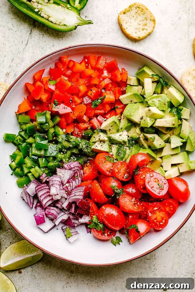 A vibrant bowl filled with diced peppers, jalapeños, tomatoes, avocado, and red onions, showcasing the fresh ingredients for the salsa.