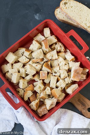 Spreading cream cheese dollops over cubed bread in a casserole dish