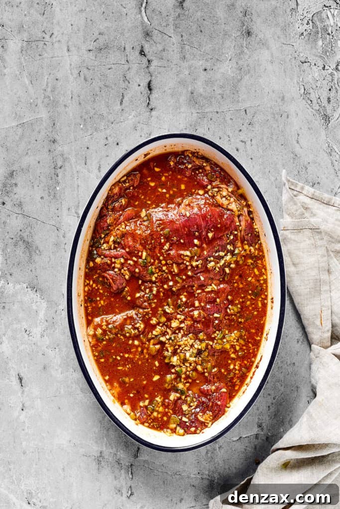Flank steak fully covered by a vibrant marinade, speckled with minced garlic and jalapeño.