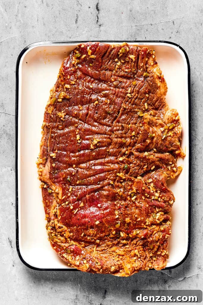 Raw, marinated flank steak resting on an enamel tray, ready for grilling.