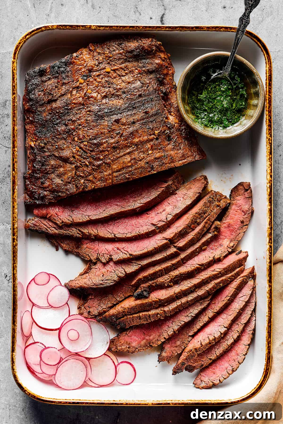 A perfectly grilled flank steak, partially sliced into thin strips, accompanied by a small cup of dipping sauce and a few slices of fresh radish.