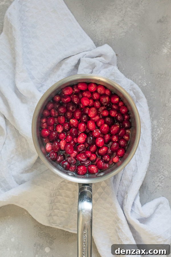 Cranberries simmering in a saucepan on a stovetop.