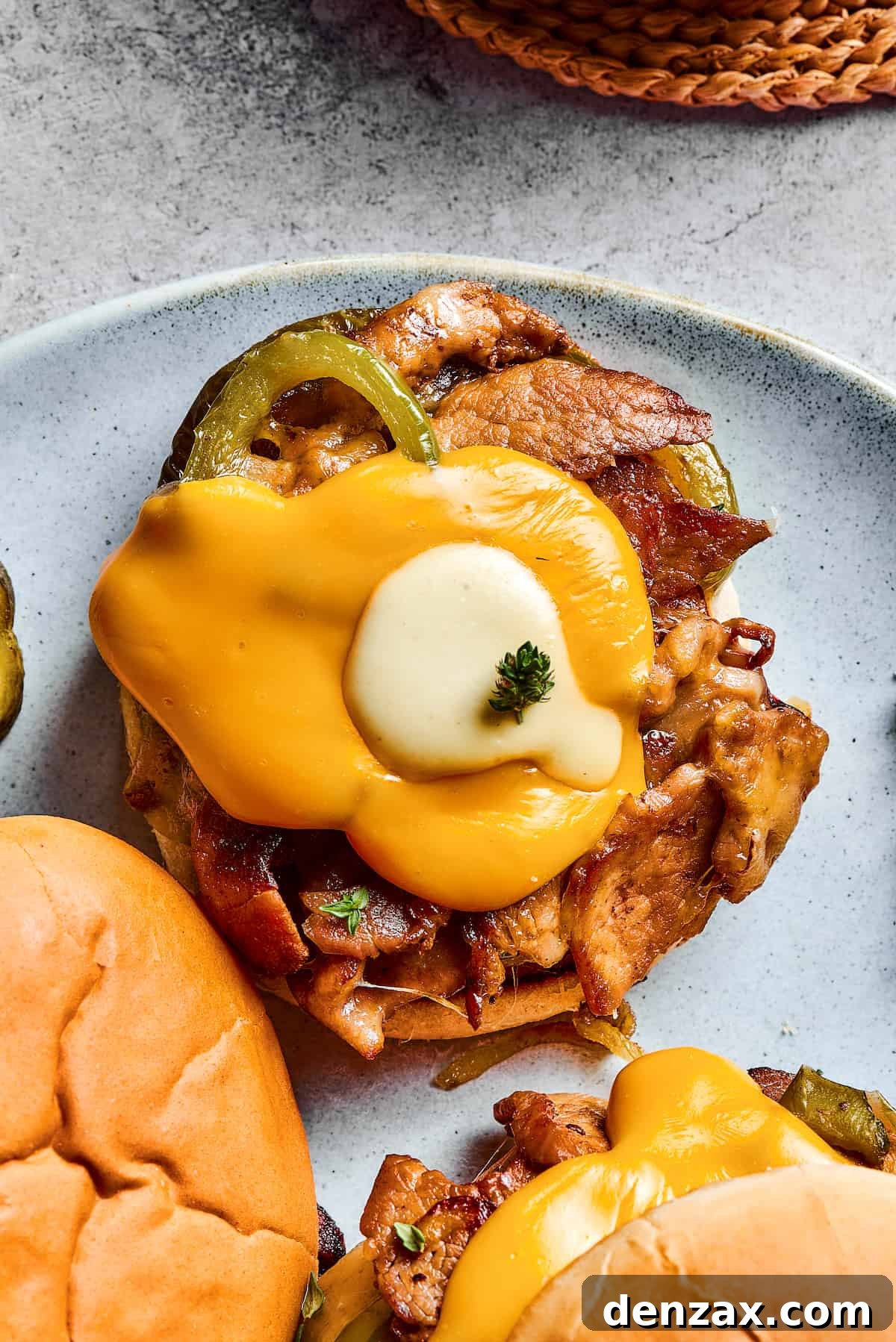 A beautifully presented Philly Cheesesteak Burger, artfully garnished with a sprig of fresh thyme and accompanied by crispy dill pickle chips, ready for a delicious meal.