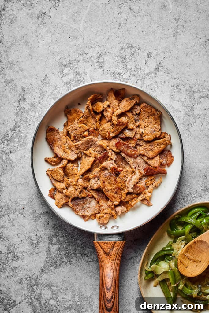 Thin strips of steak sizzle and brown in a hot skillet, cooking quickly to achieve a perfect sear for the Philly Cheesesteak Burger filling.