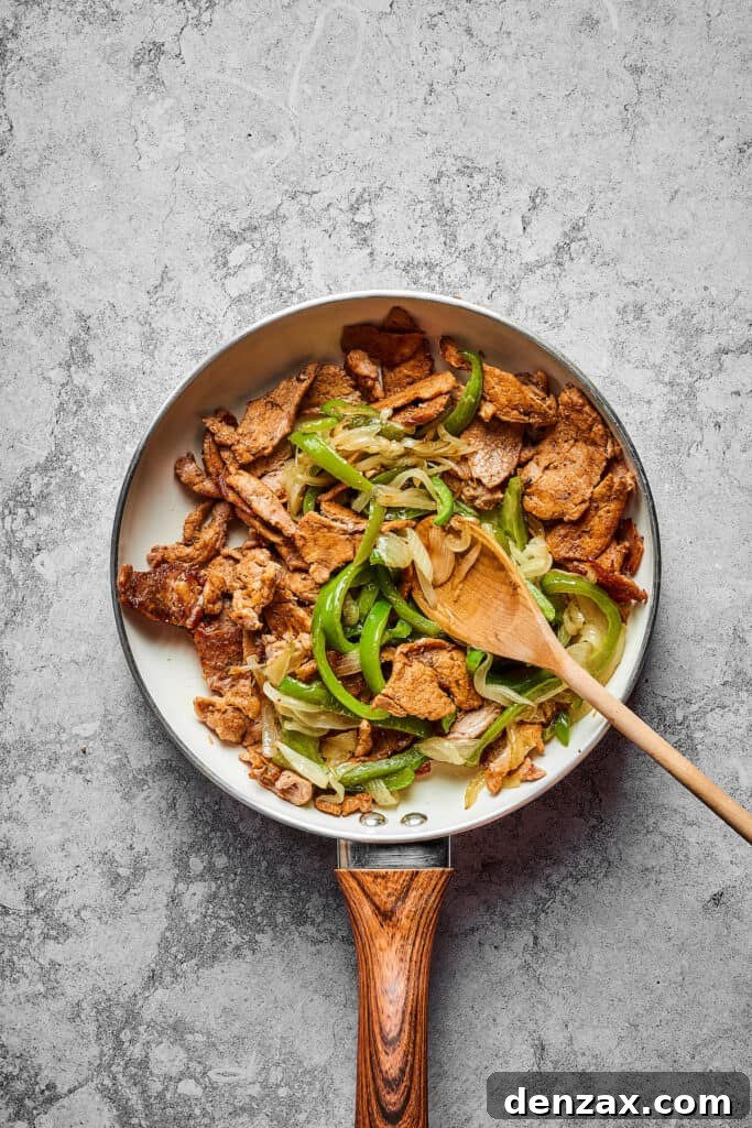 A vibrant mix of thinly sliced steak, tender onions, and crisp bell peppers cooking together in a large skillet, ready for the cheese.