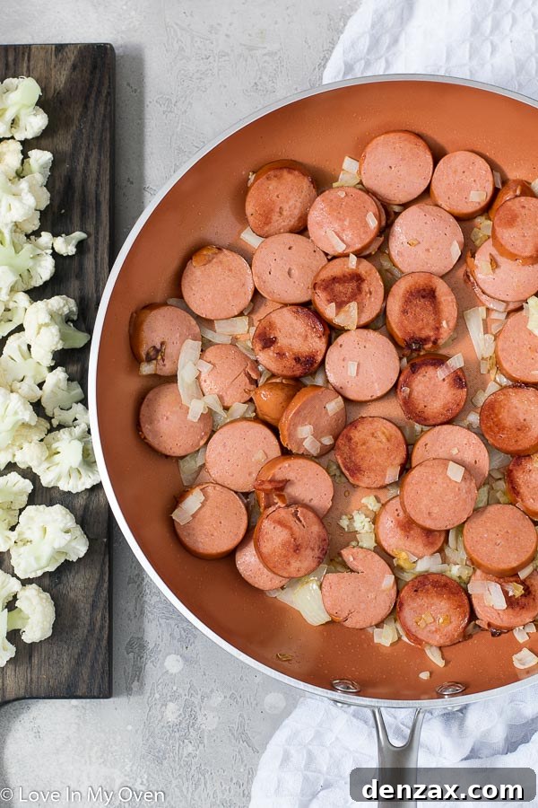 Cooking process of the Veggie and Sausage Pasta Skillet, showing pasta, cauliflower florets, and liquids simmering together in a large skillet, absorbing flavors for a creamy finish