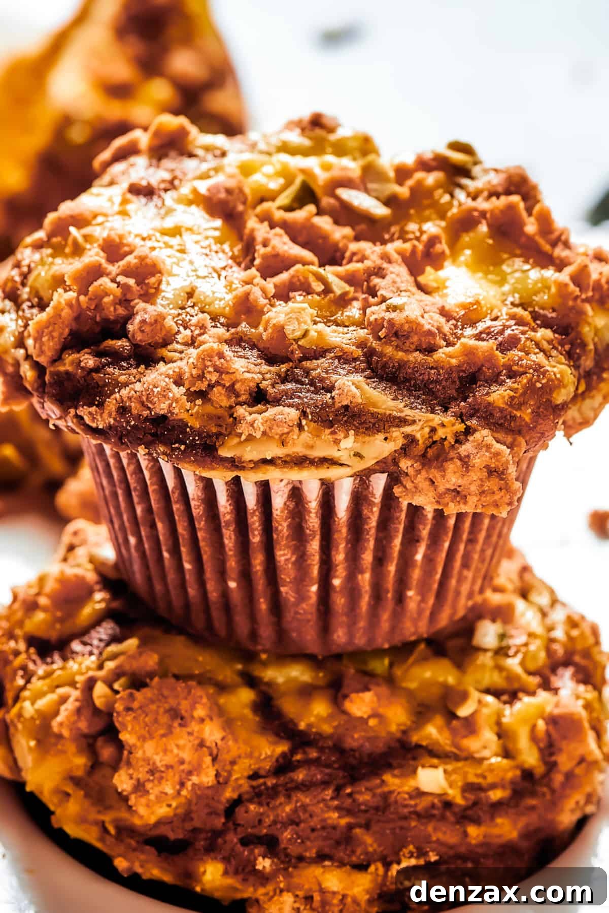A pumpkin cream cheese muffin set atop of another muffin, and arranged on a work surface.