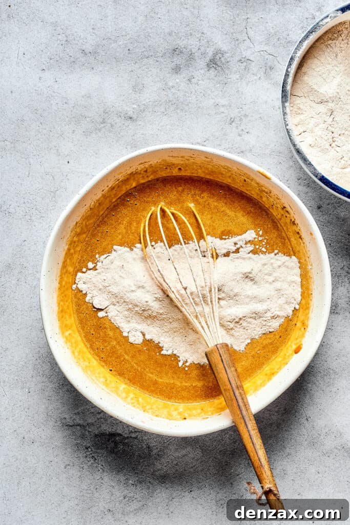 A bowl of pumpkin batter with dry ingredients and a whisk.