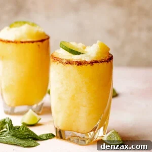 Two glasses of frozen pineapple margaritas with a chili salt rim garnished with lime and mint.