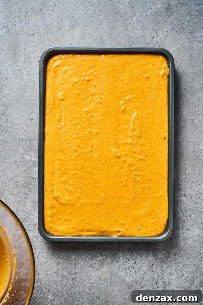 A baking dish filled with smooth pumpkin cheesecake filling, ready for streusel.