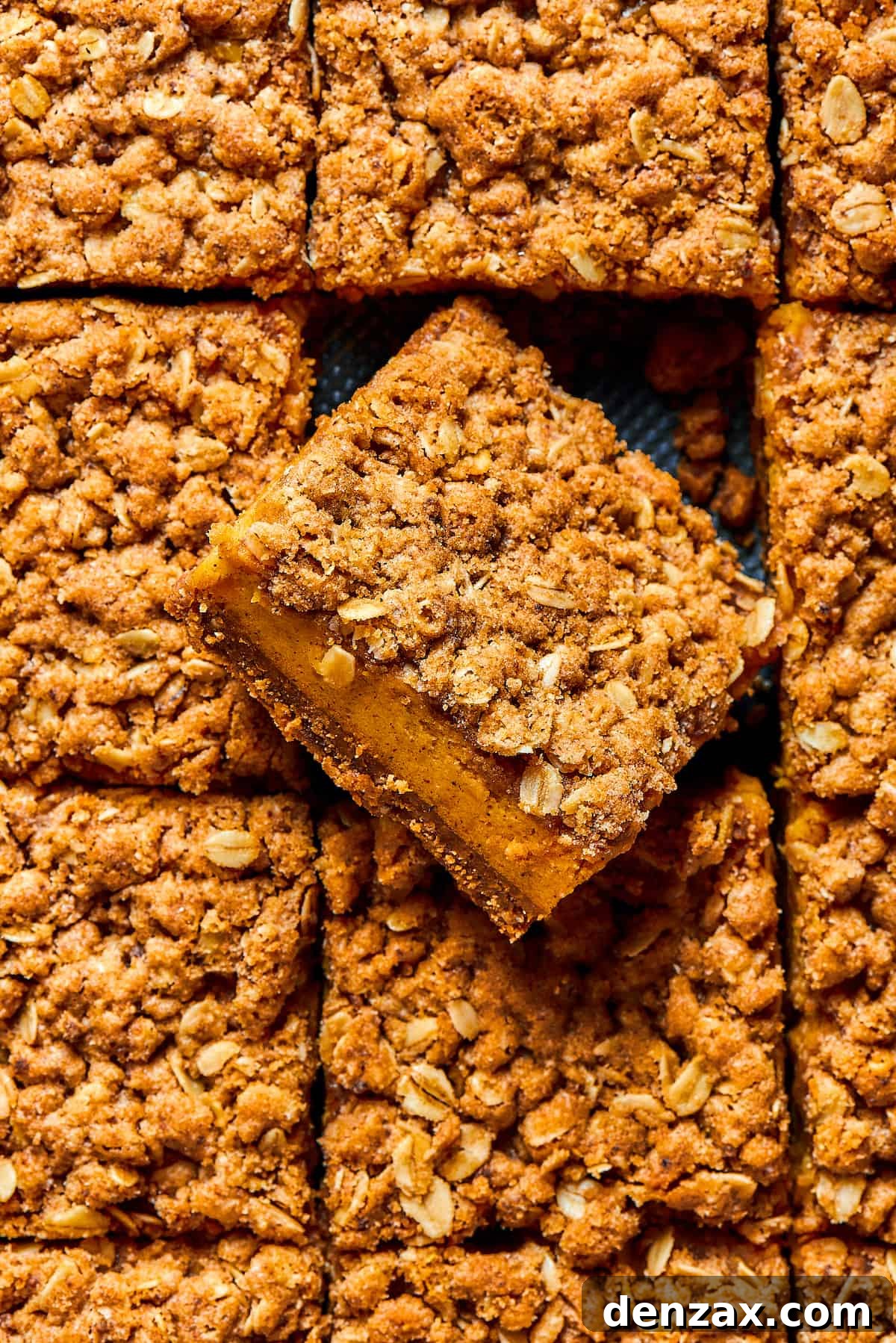 An overhead shot of pumpkin bars in a baking pan. One of the bars has been turned diagonally, to show the texture of the layers: crust, filling, and streusel.
