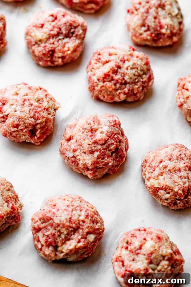 These homemade Swedish meatballs are bite-sized balls of beef and pork smothered in a rich, creamy gravy. A comforting and belly warming meal! Neatly rolled meatballs arranged on white parchment paper, ready for cooking.