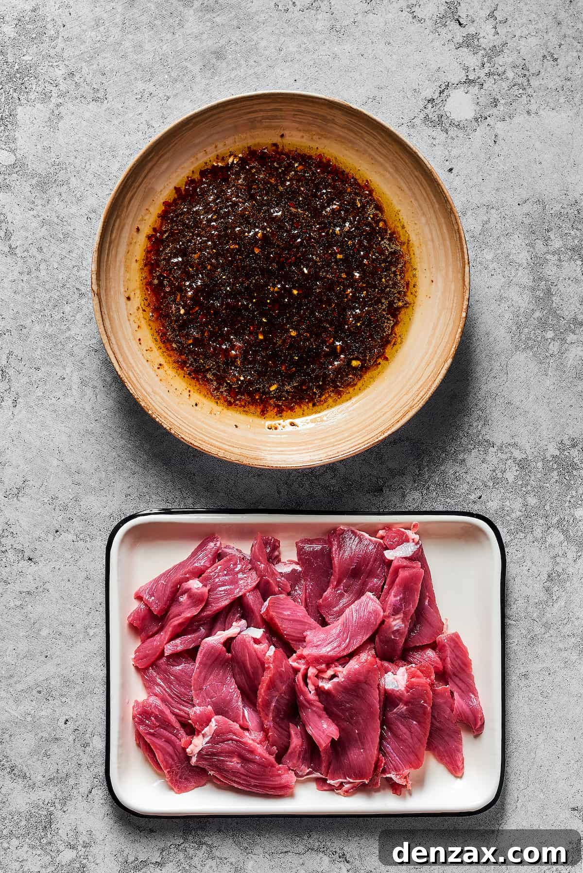 A bowl of marinade next to an enamel tray of sliced steak.