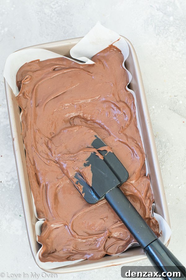 Close-up of a spatula smoothing the top of vegan chocolate ice cream in a loaf pan before freezing