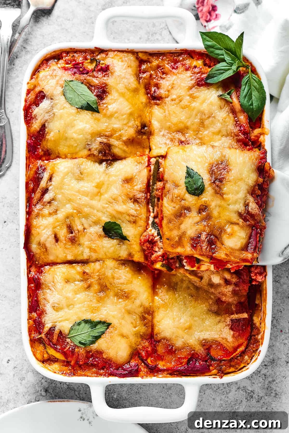 A generous serving of Zucchini Lasagna with hearty meat sauce, being lifted from a white rectangular baking dish, showcasing its perfect layers and melted cheese.