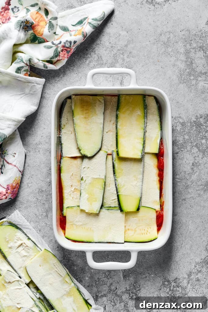 Neatly arranged strips of lightly floured zucchini forming the first layer over the rich tomato sauce in the baking dish.