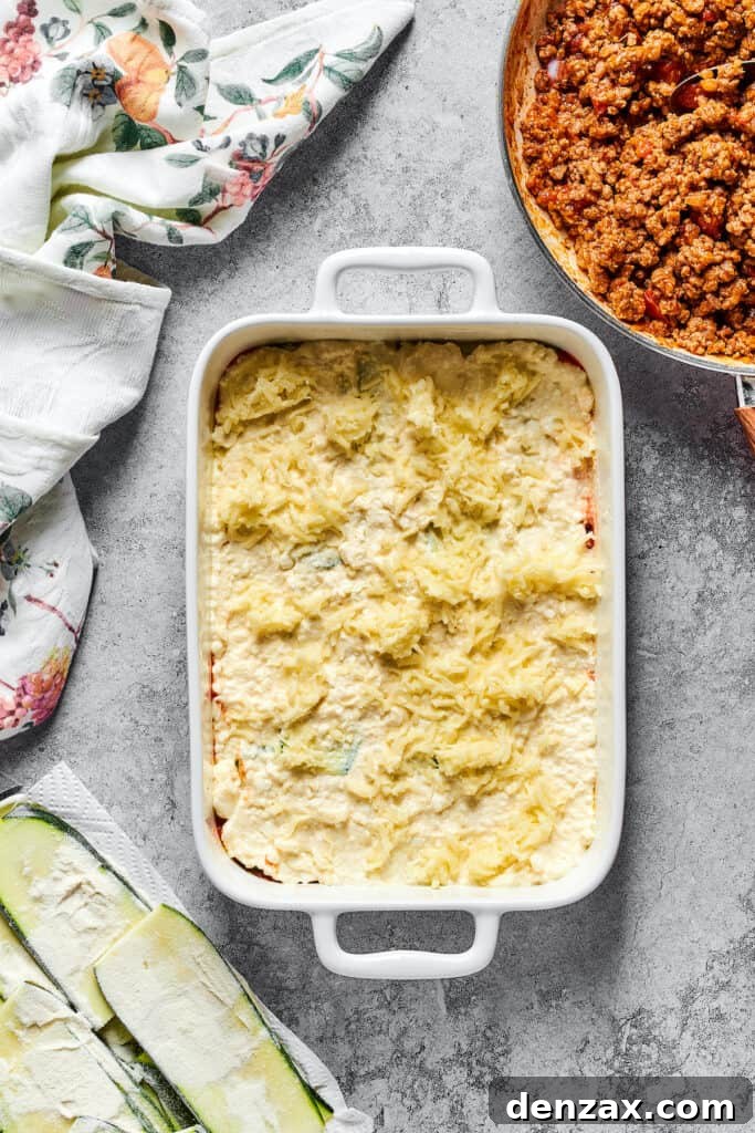 A generous dusting of shredded mozzarella cheese covering the layers of zucchini and cheese filling in the baking dish, ready for the next step.