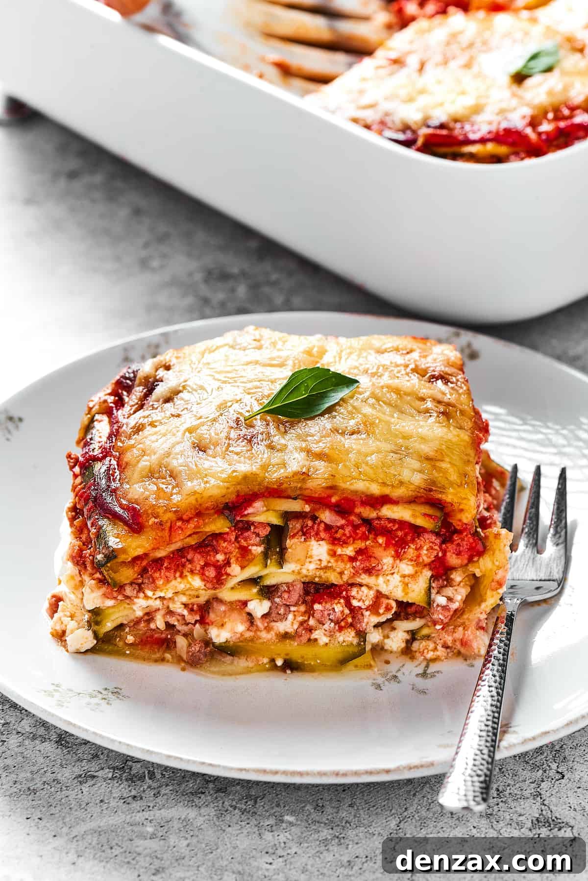 A perfectly portioned square of Zucchini Lasagna, showcasing its defined layers of zucchini, meat sauce, and cheese, served on a crisp white plate.