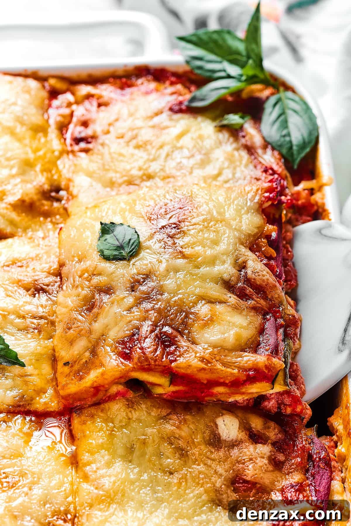 A large, comforting Zucchini Lasagna being carefully lifted out of a white rectangular baking dish, ready to be portioned and enjoyed.