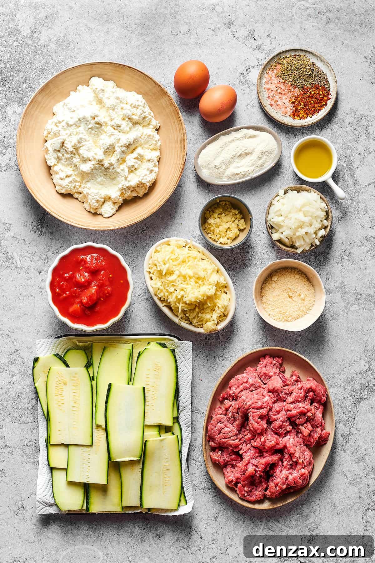 A beautifully arranged collage of all the fresh ingredients needed for Zucchini Lasagna, including cottage cheese, eggs, various seasonings, flour, olive oil, garlic, diced onion, crushed tomatoes, mozzarella, Parmesan, zucchini slices, and ground beef.