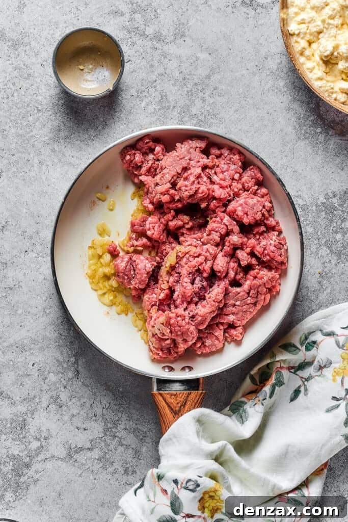 Garlic, onions, and ground beef sizzling together in a skillet, creating the aromatic base for the meat sauce.