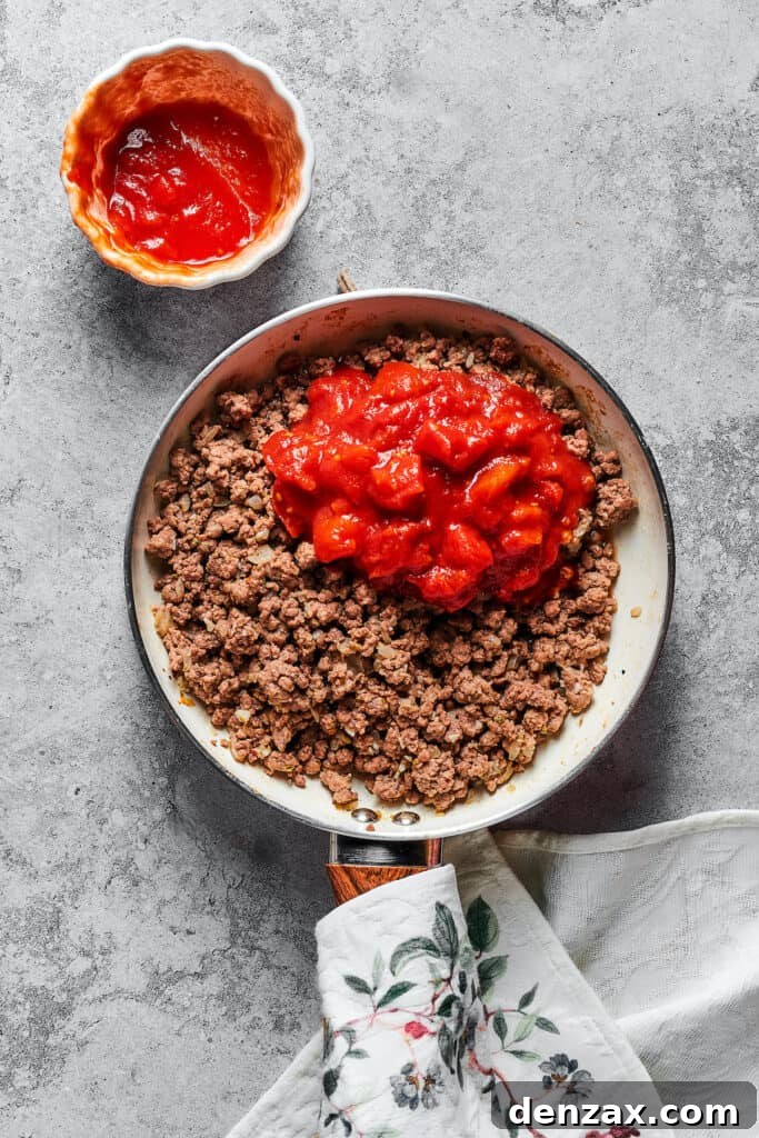 The rich, red meat sauce, brimming with crushed tomatoes and aromatic seasonings, simmering gently in a skillet.