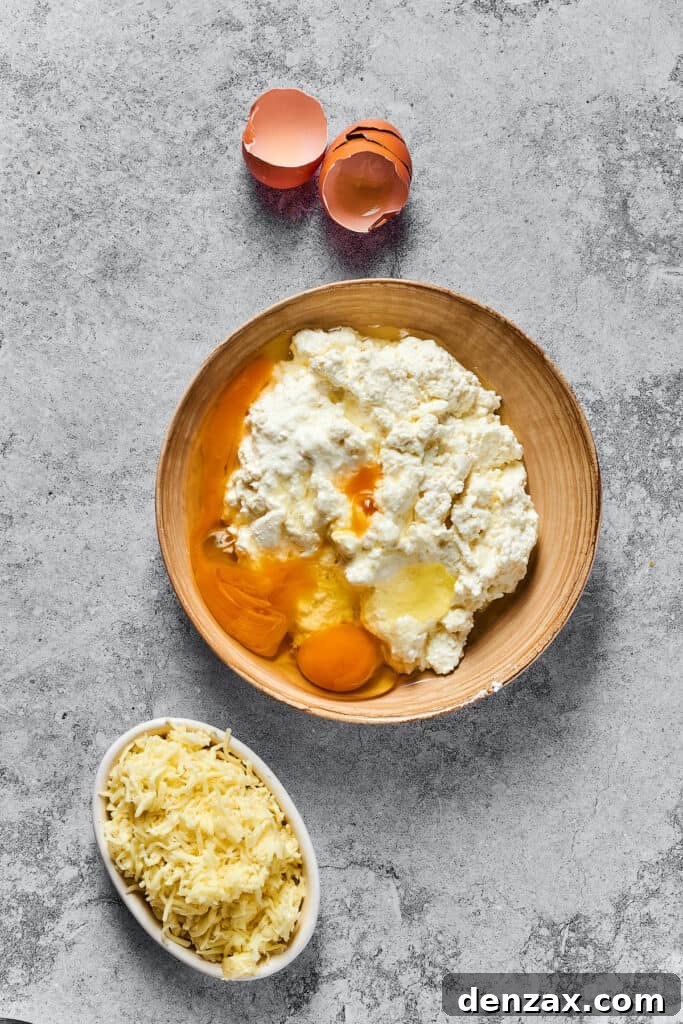 A bowl brimming with cottage cheese, Parmesan, and eggs, awaiting the final addition of mozzarella for the creamy cheese filling.