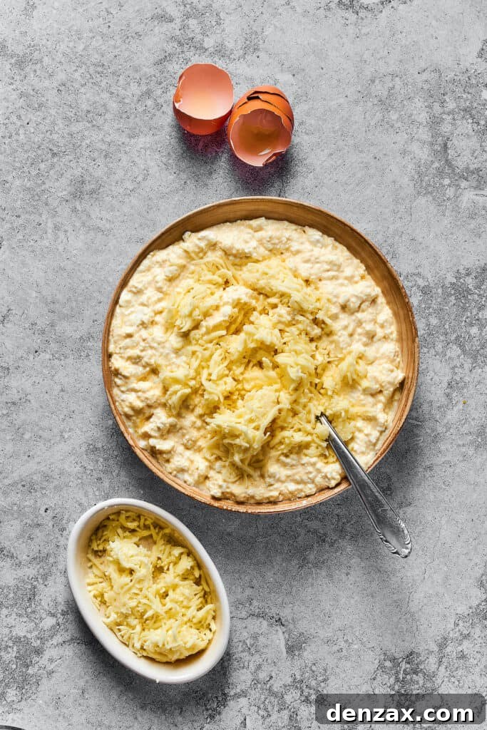 Shredded mozzarella being added to the creamy cottage cheese and egg mixture in a large bowl, completing the rich lasagna filling.