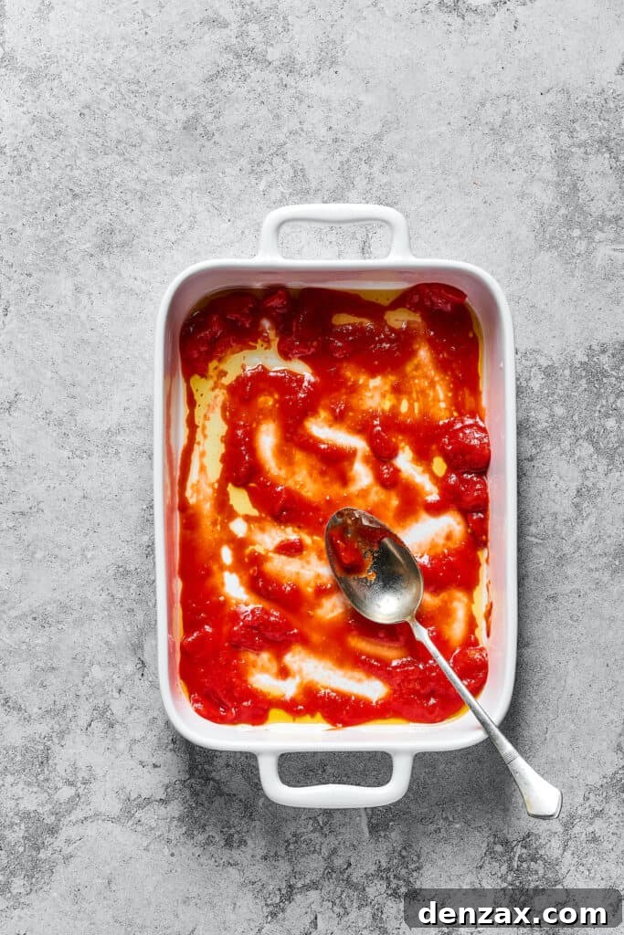 A vibrant red layer of tomato sauce spread evenly across the bottom of a white baking dish, preparing for the lasagna layers.