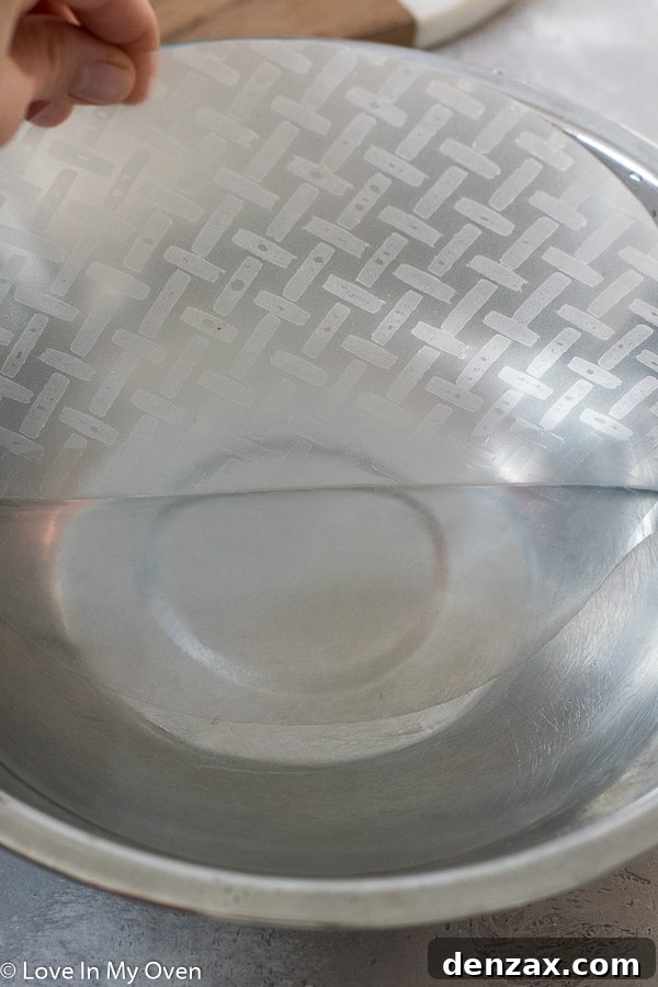 Rice paper being dipped in warm water and then laid flat on a cutting board, ready for filling.