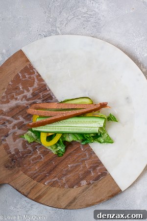Two hands demonstrating the folding and rolling process of a turkey pepperoni salad roll on a cutting board.