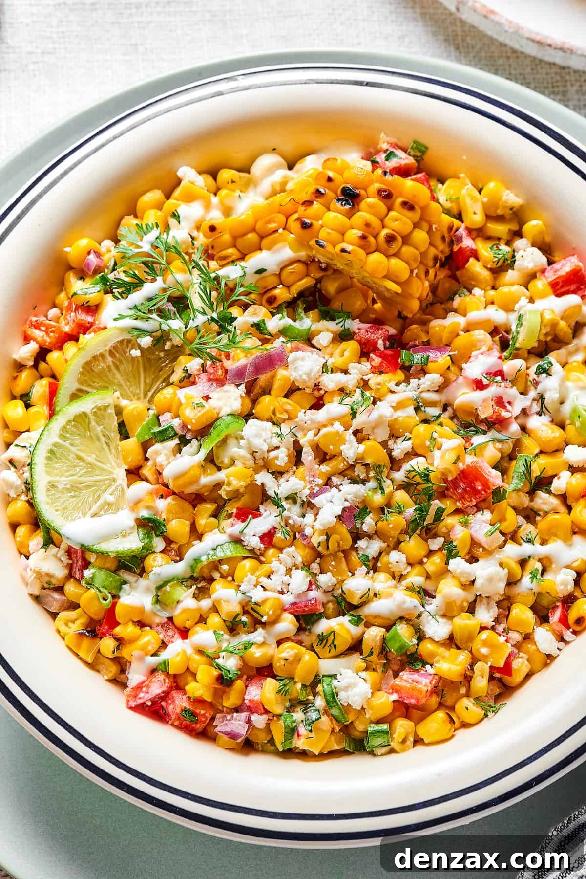 A vibrant bowl of Mexican street corn salad, showcasing grilled corn kernels, red bell peppers, cilantro, and a creamy dressing, garnished with fresh lime.