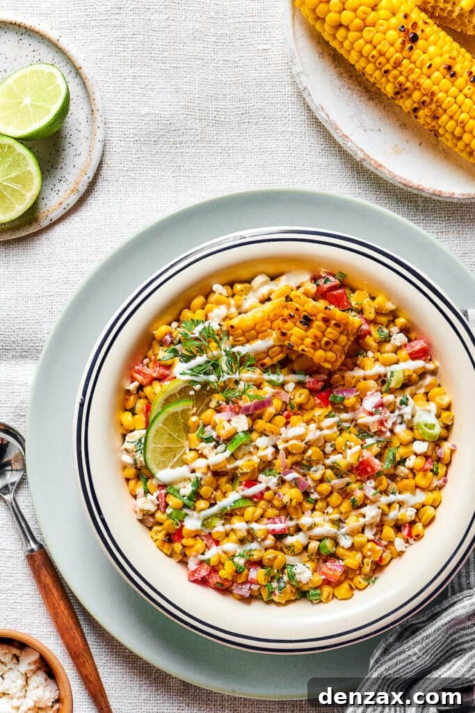 Mexican street corn salad in a serving bowl, beautifully garnished with extra dressing, lime wedges, and cilantro.