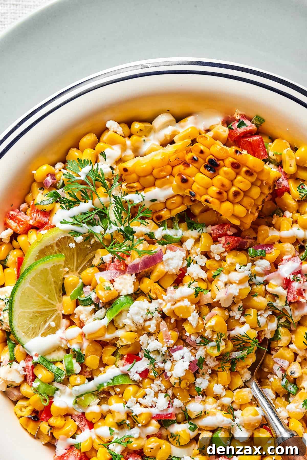Close-up shot of grilled corn salad with creamy dressing, lime wedges, and chopped herbs, highlighting the vibrant textures.