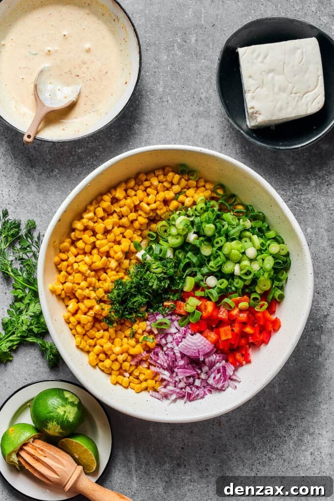 Elote salad ingredients, including grilled corn, bell peppers, onions, and herbs, in a bowl before the dressing is added.