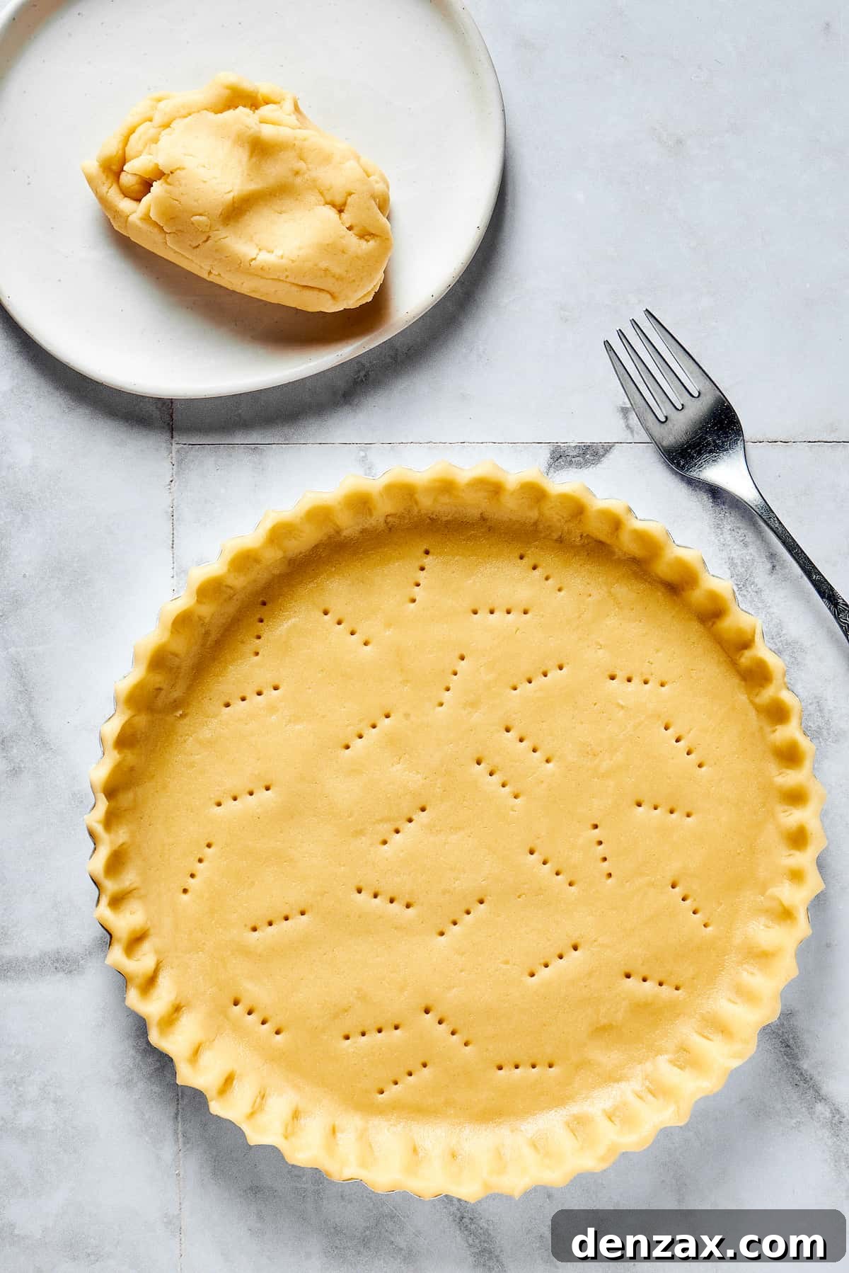 Golden-brown, flaky pie dough pressed into a pie dish with elegantly crimped edges. The crust has been expertly pricked with a fork, ready for baking.