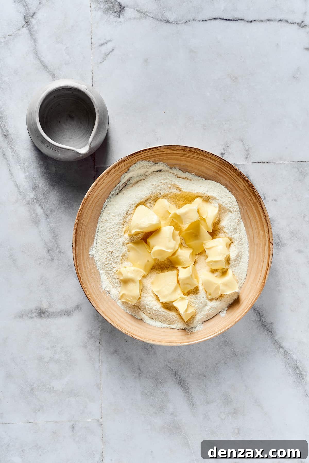 Small cubes of cold butter being dropped into a mixing bowl filled with dry baking ingredients (flour, sugar, salt).