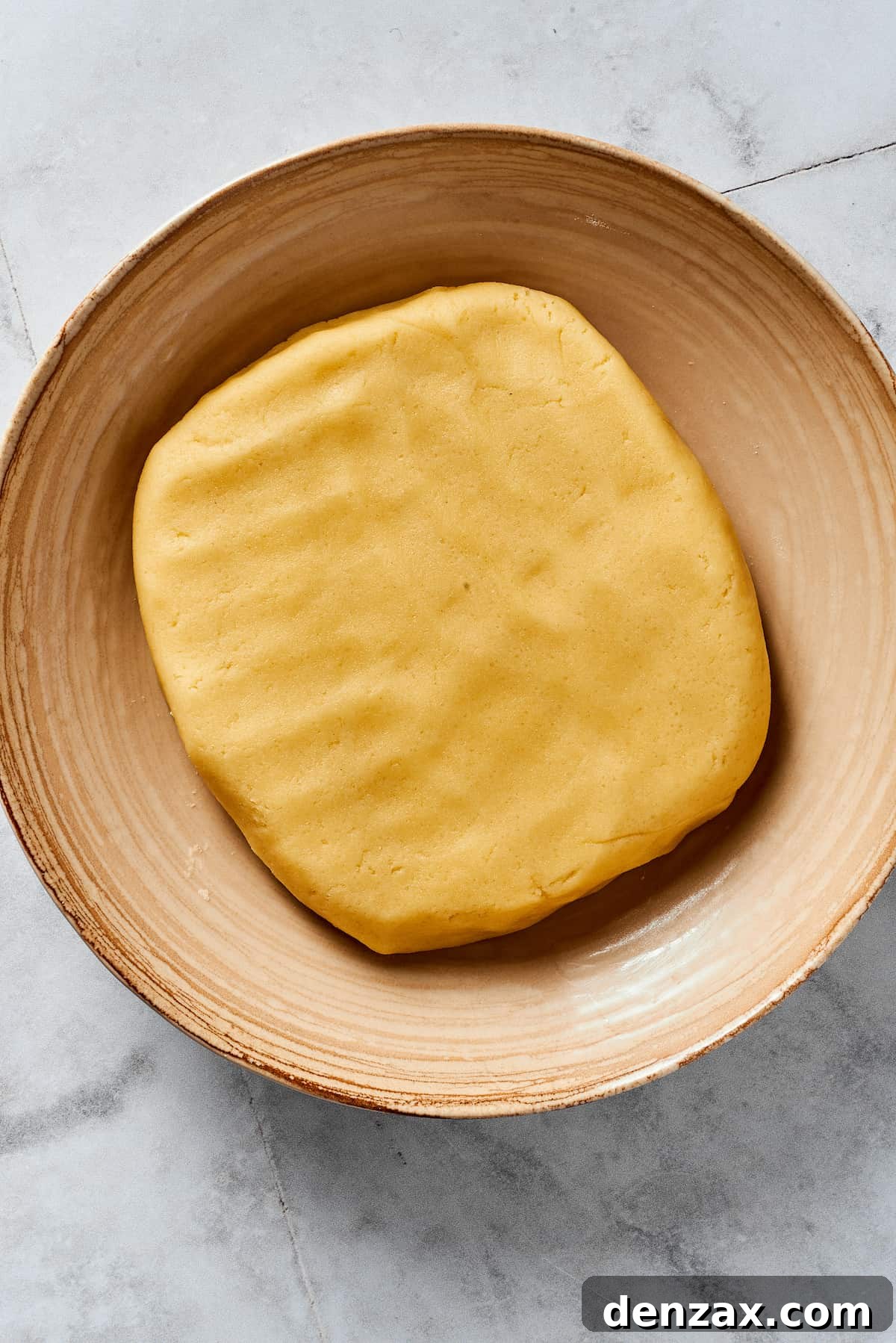 A flattened, disc-shaped piece of pie dough resting inside a mixing bowl, after ice water has been added and the dough has just come together.